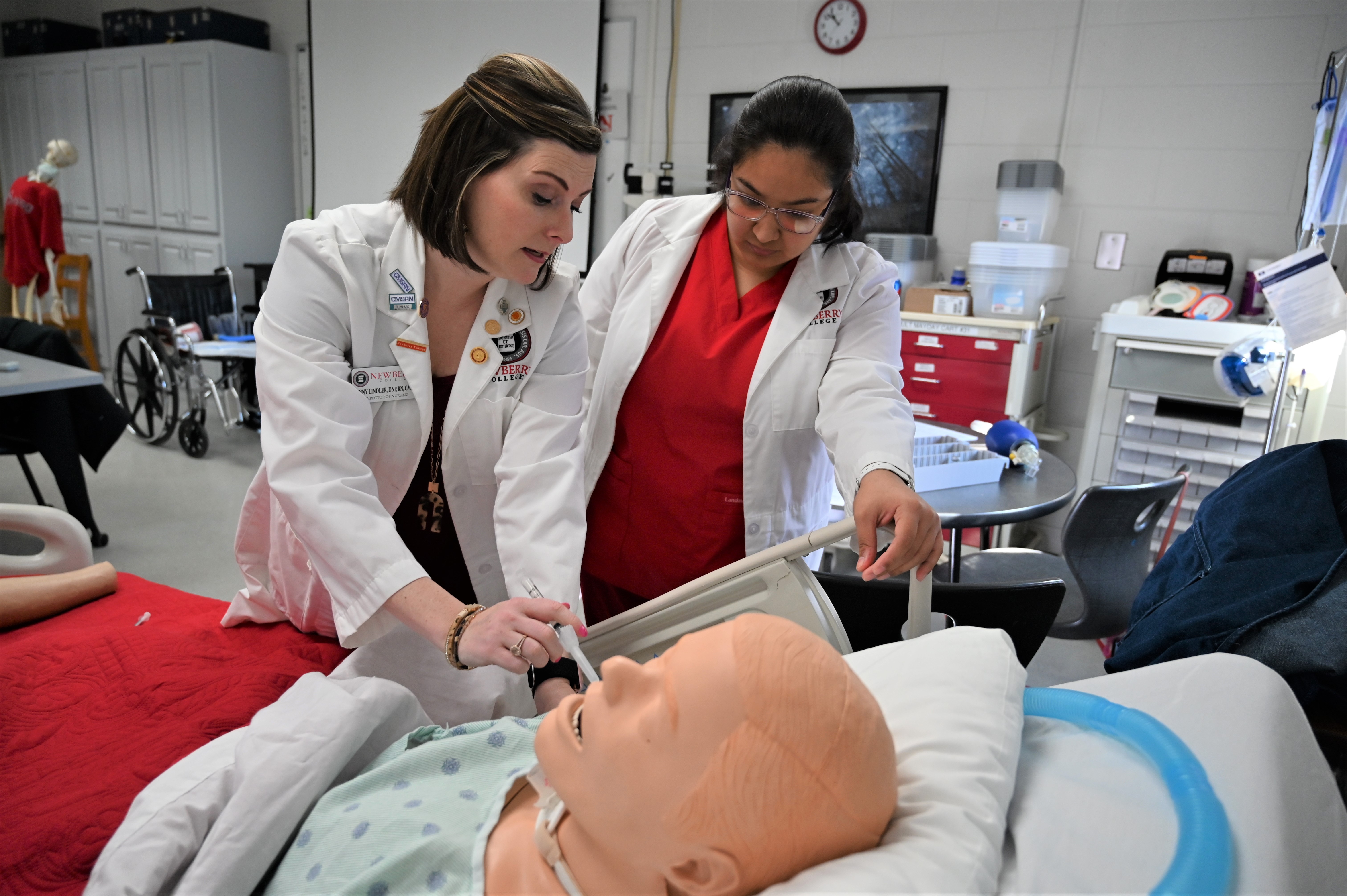 A nursing instructor and nursing student examine a model patient together in a clinical setting