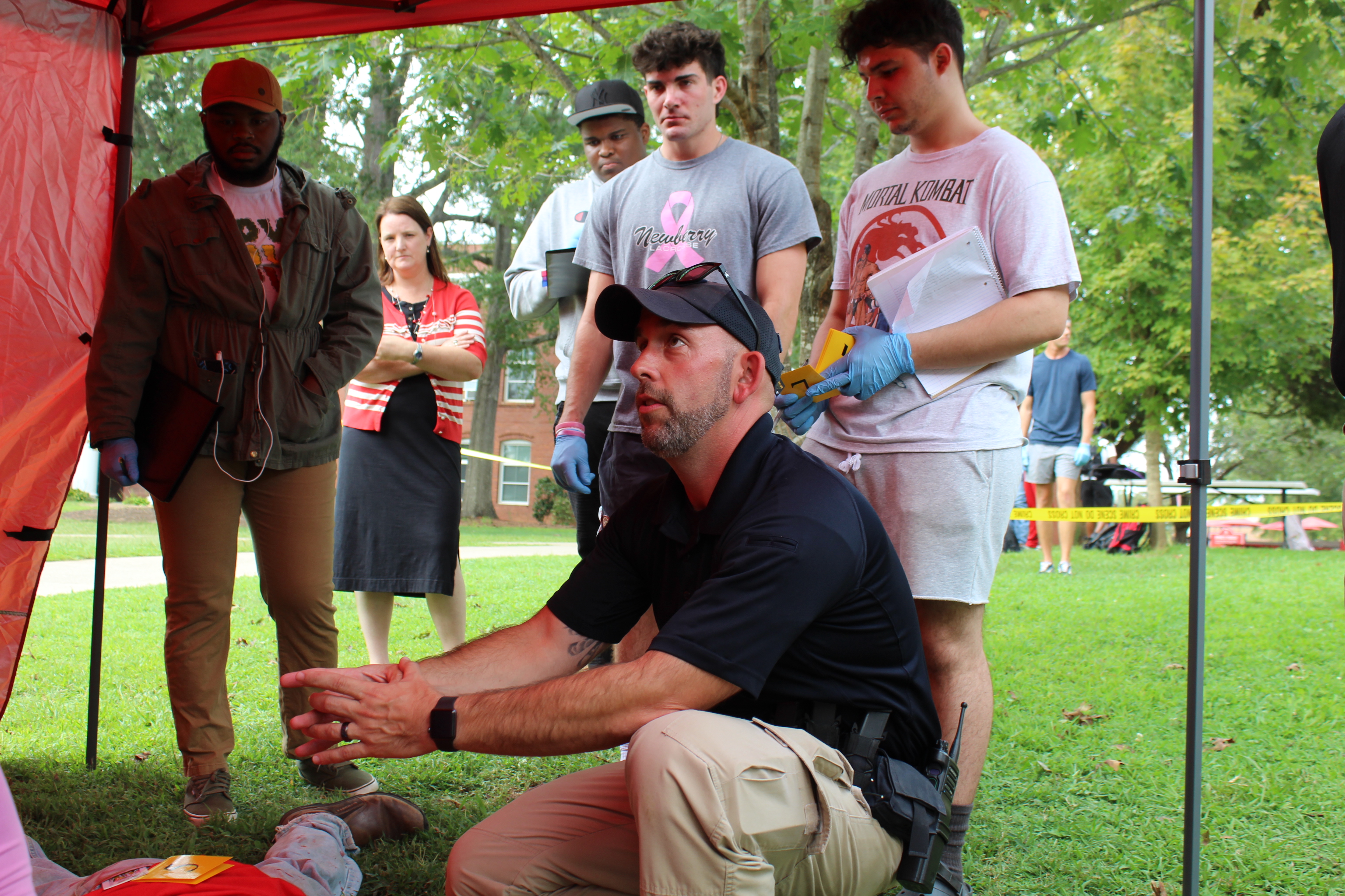 A police officer kneels to instruct students at a mock crime scene