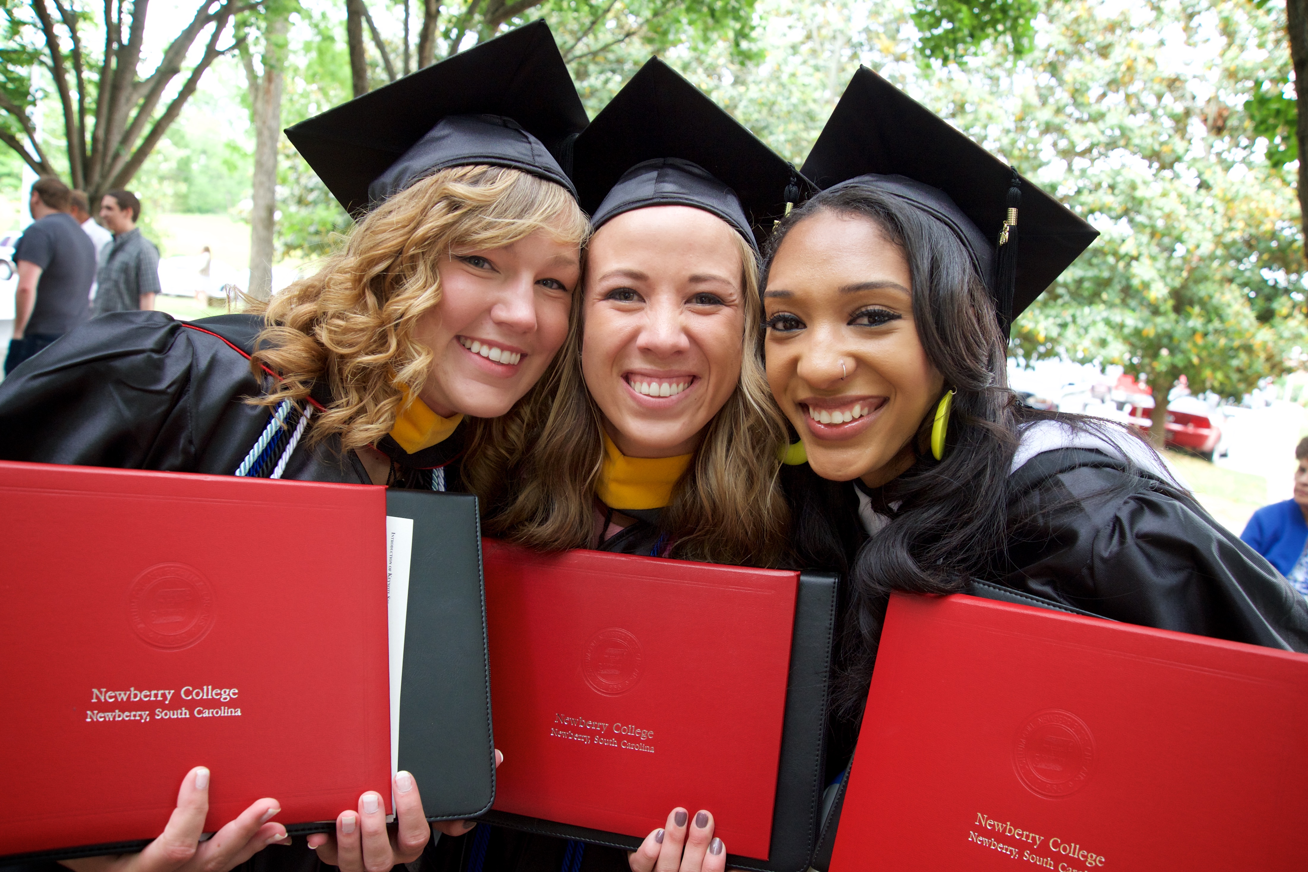 Three graduates holding up diplomas